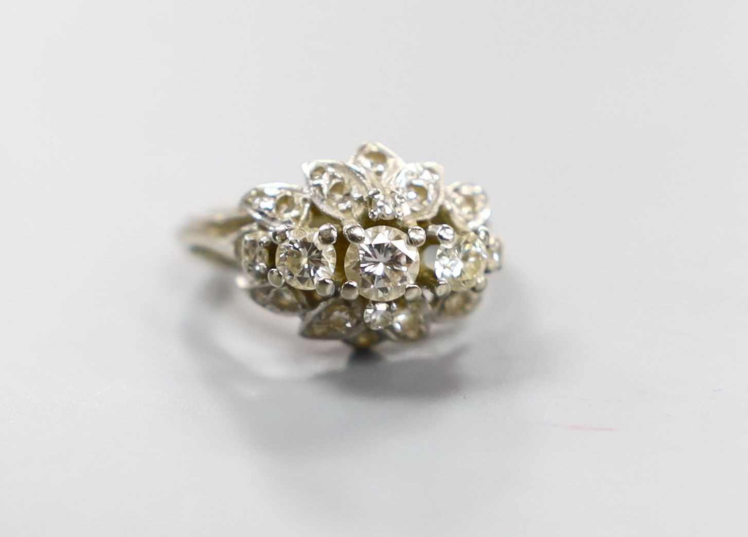 A white metal and three stone diamond ring with diamond cluster setting, size M, gross weight 4.4 grams.